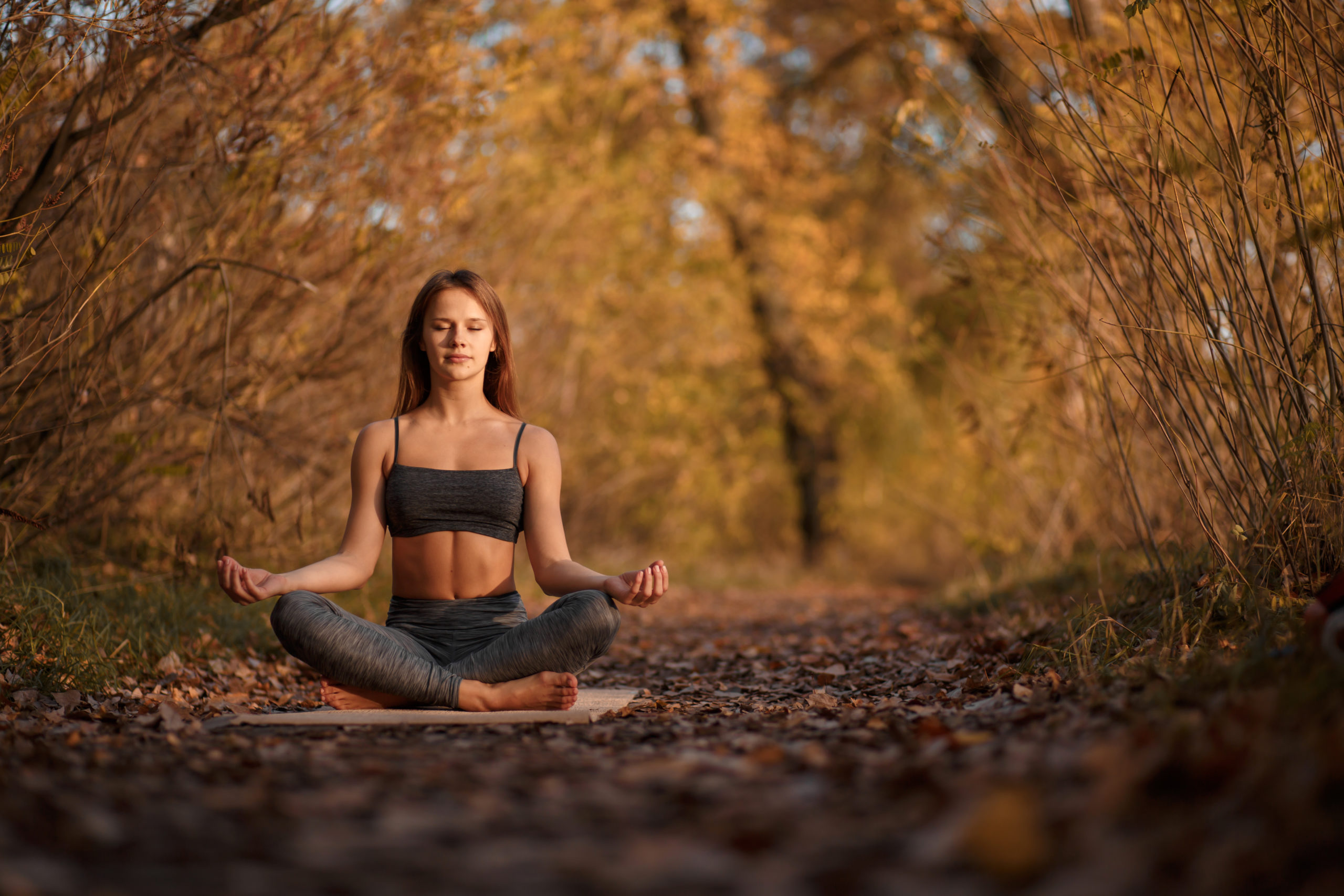 Young woman practicing yoga exercise at autumn park with yellow