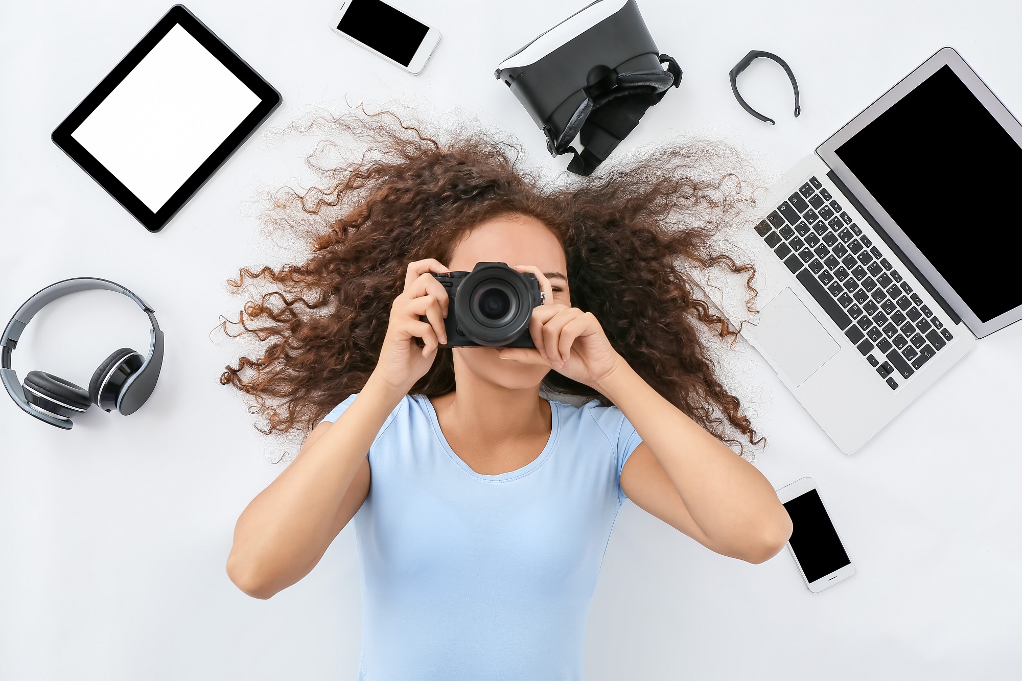 Young woman with different gadgets and photo camera on white bac